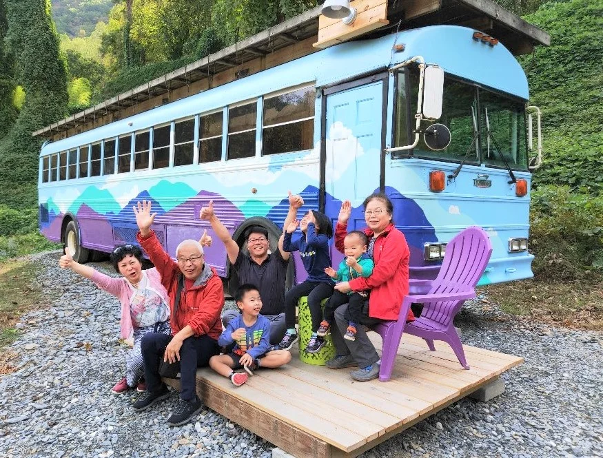 Family waving in front of the Travel-Inn Skoolie bus